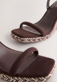 Sandale platformă din piele întoarsă maro, cu două barete subțiri, talpă texturată din țesătură cu model chevron în nuanțe deschise și închise.
