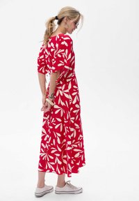 Rotes Maxikleid mit weißem Blattmuster, kurzen Ärmeln und tailliertem Bund. Kombiniert mit weißen Turnschuhen. Glatte Stofftextur.