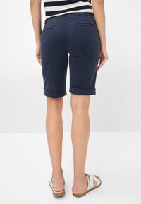 Marineblaue Shorts mit aufgekrempelten Säumen, aus weichem Stoff gefertigt, mit Gesäßtaschen und einem dezenten Logo-Detail über der rechten Tasche.