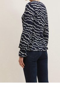 Navy blouse with white wavy patterns, long sleeves with elastic cuffs, and a peplum waist design. Fabric appears lightweight and textured.