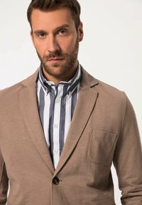 Blazer beige con un solo bottone, tessuto testurizzato e taschino sul petto, abbinato a una camicia a righe blu e bianche.