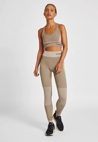 Beige sport-bh och tajta leggings gjorda av strukturerat tyg. Leggingsen har varierande nyanser och färgblock. Svarta sportskor.