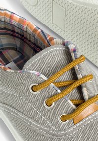 Baskets en toile grises avec lacets orange, doublure intérieure en plaid, couture blanche et semelle en caoutchouc. Équipées d'œillets métalliques et d'un accent beige.