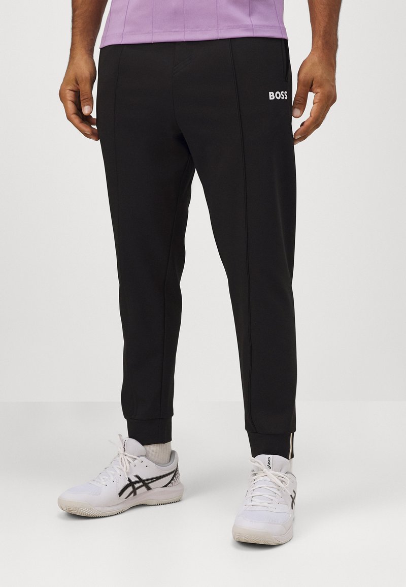 Schwarze Jogginghosen mit schlanker Passform, versehen mit einem weißen "BOSS"-Logo und Reißverschlussdetails an den Knöcheln. Hergestellt aus glattem, elastischem Material.