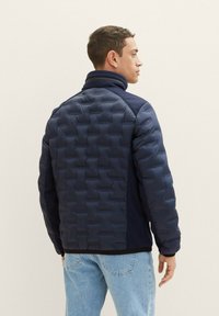 Giacca imbottita blu marina con un design trapuntato e texture. Presenta un fit aderente e tessuto liscio a contrasto sui lati.