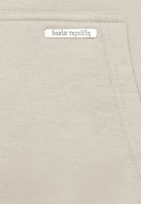 Vaalean beige pullover-huppari, jossa on tasku ja hopeinen metallilappu, jossa lukee "bazix republiq". Pehmeä kangas, jossa on sileä pinta.