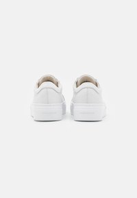 Baskets blanches en cuir avec une texture lisse, une forme arrondie et une semelle en caoutchouc blanche avec un logo discret sur le talon.