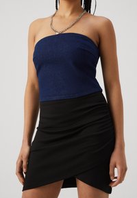 Dunkelblaues, trägerloses Denim-Top, kombiniert mit einem schwarzen, strukturierten Minirock mit Rüschen und asymmetrischem Saum. Silberne Kette als Akzent.