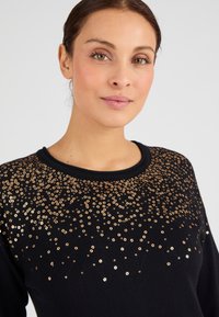 Maglione nero con scollo rotondo, decorato con paillettes dorate di diverse dimensioni disposte in un motivo a gradiente nella zona del petto.