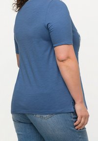 Blå kortärmad topp med avslappnad passform, med rund halsringning och sidslitsar, i kombination med denimjeans. Slät textur.