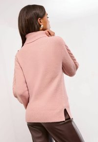 Rosa gestrickter Pullover mit hohem Kragen, strukturiertem Stoff und seitlichen Schlitzen. Mit gerippten Bündchen und lockerer Passform.
