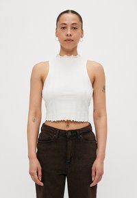 Hvit croppet topp med høy volangkrage og vertikal ribbet tekstur, sammen med mørkebrune høyt midje jeans.