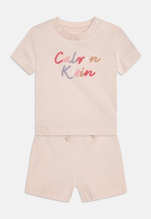 Lyserød bomulds to-dels sæt bestående af en T-shirt med korte ærmer, der har flerfarvet "Calvin Klein" tekst, og matchende shorts med elastisk talje.