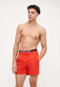 Shorts de bain rouges en tissu léger, dotés d'une ceinture élastique noire avec le logo "CALVIN KLEIN" et d'un cordon de serrage.