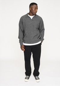 Grå ribbet trøje med krave, parret med sorte bukser og sort-hvide sneakers. Modellen står foran en ensfarvet hvid baggrund.