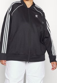 Mustat vetoketjuhuppari, jossa on valkoiset kolmiosta raidat hihoissa. Varustettu pyöreällä kaula-aukolla, sivutaskuilla sekä resorikäänteillä hihansuissa ja helmassa.