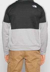 Giacca a pullover nera e grigia con un design testurizzato, tessuto a coste nella sezione inferiore e un logo sulla parte superiore della schiena.