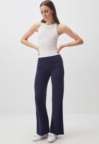 Top bianco senza maniche, aderente. Pantaloni a campana blu navy, texture liscia. Sneakers bianche. Design minimalista, eleganza sottile.
