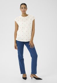 Haut crème à manches courtes avec des motifs de cœurs rouges, associé à un jean droit bleu et des escarpins slingback noirs à bout pointu. Design simple.