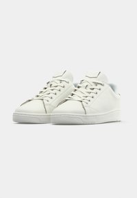 Bílé kožené tenisky s kulatou špičkou, plochou gumovou podrážkou a jednoduchým designem na šněrování, který obsahuje decentní švy a texturovaný jazyk.