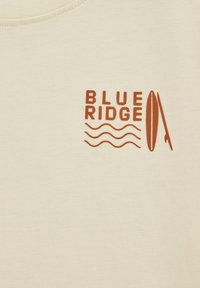 Kremowa koszulka bawełniana z nadrukiem "BLUE RIDGE" w ciemnopomarańczowym kolorze, z falistymi liniami i wzorem deski surfingowej. Krótki rękaw, okrągły dekolt.