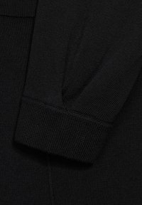 Tejido de suéter negro de punto con detalle de puños acanalados. La textura es fina y de tejido uniforme, con un diseño limpio y sencillo.