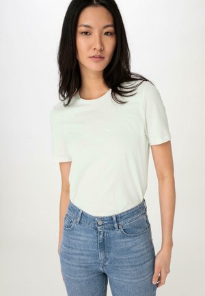 Hellgrünes T-Shirt mit kurzen Ärmeln aus weichem Stoff, kombiniert mit hochgeschnittenen blauen Jeans aus Denim mit klassischer Passform und dezentem Verblassen.