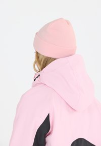 Vaalea vaaleanpunainen takki hupulla, jossa on mustia yksityiskohtia ja sileä pinta. Yhdessä vastaavan vaaleanpunaisen neulottavan pipon kanssa asu on täydellinen.