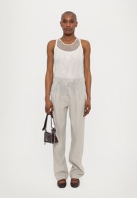 Lichte zilveren mesh tanktop met geplooide details aan de zoom, gecombineerd met lichtgrijze wijde broek en een kleine donkere handtas.