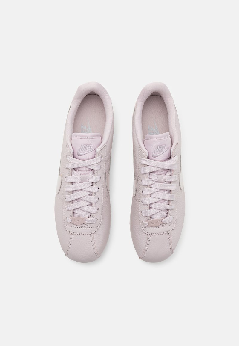 Zapatillas de piel de color rosa claro con una textura suave, puntera redonda y cordones planos. Presentan un sutil logotipo en la lengüeta y el costado.