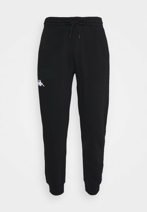 Schwarze, zulaufende Jogginghosen mit elastischem Bund und Kordelzug, mit kleinem weißen Logo am linken Oberschenkel vor weißem Hintergrund.