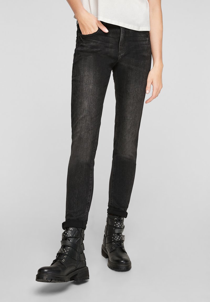 Jeans en denim noir avec une coupe slim, présentant une texture délavée et un design à cinq poches, associés à des bottes de combat noires ornées de garnitures en argent.
