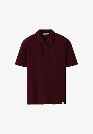 Polo bordeaux à manches courtes en tissu texturé, patte à trois boutons, et petite étiquette blanche au bas de l’ourlet.