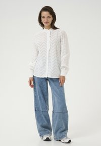 Wit overhemd met chevronpatroon, gerimpelde sluiting, lange mouwen, gecombineerd met losse, lichtblauwe denimjeans en sneakers.
