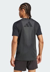 T-shirt de sport noir à manches courtes, avec un motif dégradé au dos et un logo Adidas en gris foncé en haut à gauche.