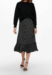 Suéter negro combinado con una falda hasta la rodilla que presenta un estampado de cebra en negro y gris, con tejido texturizado y un dobladillo con volantes. Sandalias negras de tacón.