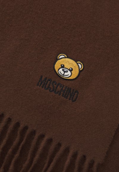 Sciarpa marrone realizzata in morbido tessuto, con un design di un orso ricamato in giallo e nero, accompagnato dal testo "Moschino" in basso. Bordo frangiato.