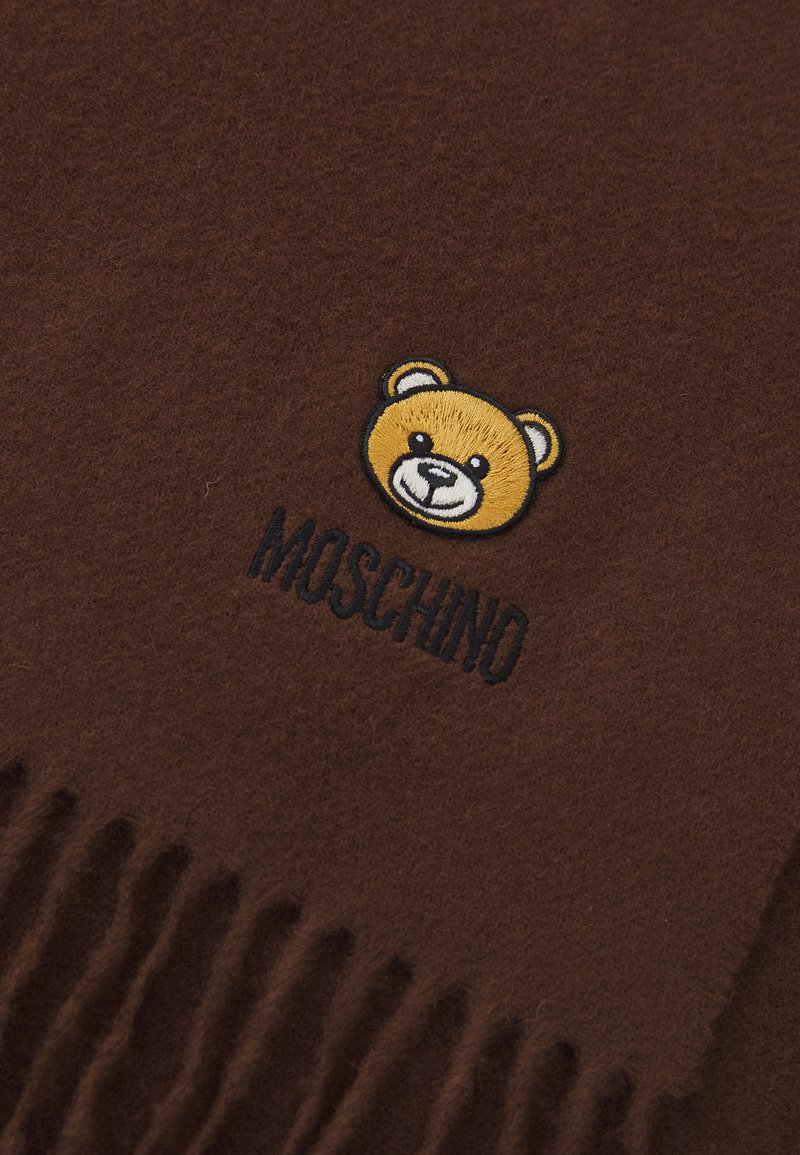 Brun uld scarf med en broderet bjørne grafik i gult og sort, med "Moschino" tekst nedenfor og frynser i kanten.