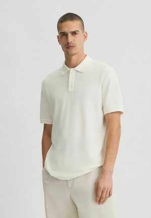 Polo a maniche corte color avorio, realizzato in tessuto morbido, con una pattina a tre bottoni e un logo ricamato discreto sul petto.