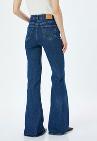 Jeans in denim blu svasati con vita alta, cinque tasche, una patch in pelle sul retro e una finitura testurizzata.