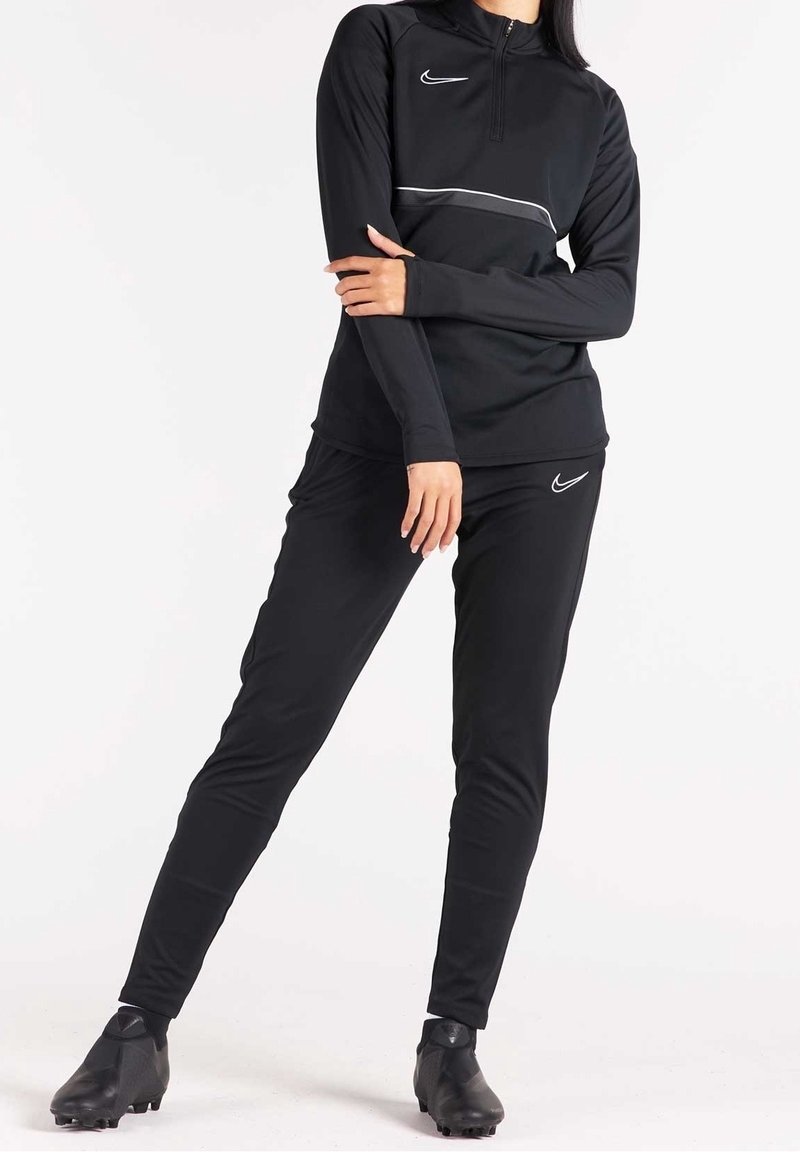 Conjunto deportivo negro que incluye una camiseta de manga larga con media cremallera y un par de pantalones ajustados a juego, ambos con un logo y detalles en blanco.