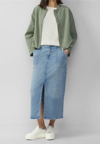 Ljusgrön bomberjacka, vit texturerad stickad tröja, blå denim-maxikjol med frontslits och vita sneakers. Avslappnad, lager-på-lager-look.