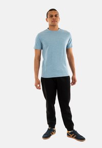 Light blue short-sleeve t-shirt paired with black sweatpants and black sneakers featuring orange accents. Simple, casual fit with a round neckline.