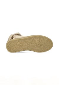 Botín de ante beige con suela de goma texturizada, que presenta una forma redondeada y un diseño sencillo. La vista inferior muestra los detalles de la suela.