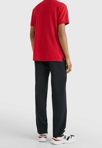 Röd kortärmad polo shirt med sidoflikar, matchad med mörka byxor och vita sneakers med röda och marina inslag.