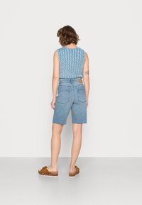 Blå stickad ärmlös topp med ett strukturerat mönster, kombinerad med ljusblå denimshorts med fransig fåll och bakfickor. Bruna slip-on skor.