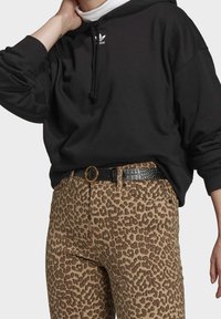 Svart hoodie med dragsko och vit logotyp, i kombination med bruna leopardmönstrade byxor och ett svart bälte i krokodilstruktur med guldspänne.