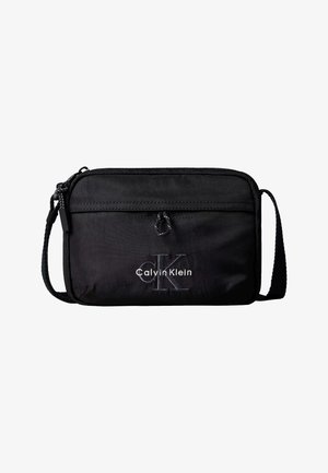 Czarna torba na ramię Calvin Klein z przednią kieszenią na suwak i regulowanym paskiem, z wyhaftowanym logo i małą tkaną pętelką nad kieszenią.
