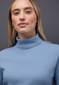 Jasnoniebieski sweter typu golf wykonaną z materiału prążkowanego. Projekt charakteryzuje się wysokim kołnierzem oraz dopasowanym krojem z delikatną teksturą.