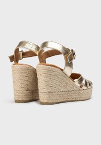 Sandales en métal doré à talons compensés en jute tressé, avec des sangles réglables à boucle et des orteils ouverts, présentant une finition texturée et un design superposé.